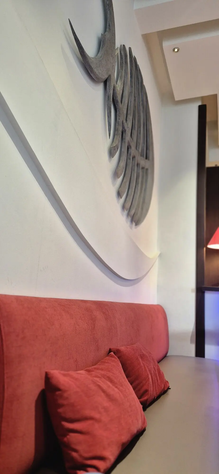 Banquette rouge et coussins sous la décoration murale en arête